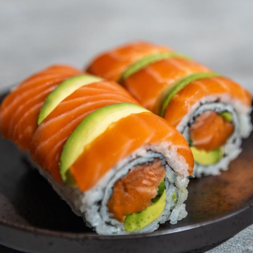 Two Iro Sushi "Stuff x Roll" sushi rolls, topped with salmon and avocado, on a dark plate.