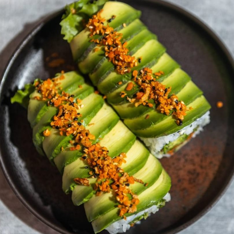 Two Iro Sushi Stuff x Roll sushi rolls, topped with avocado slices and crunchy orange garnish.