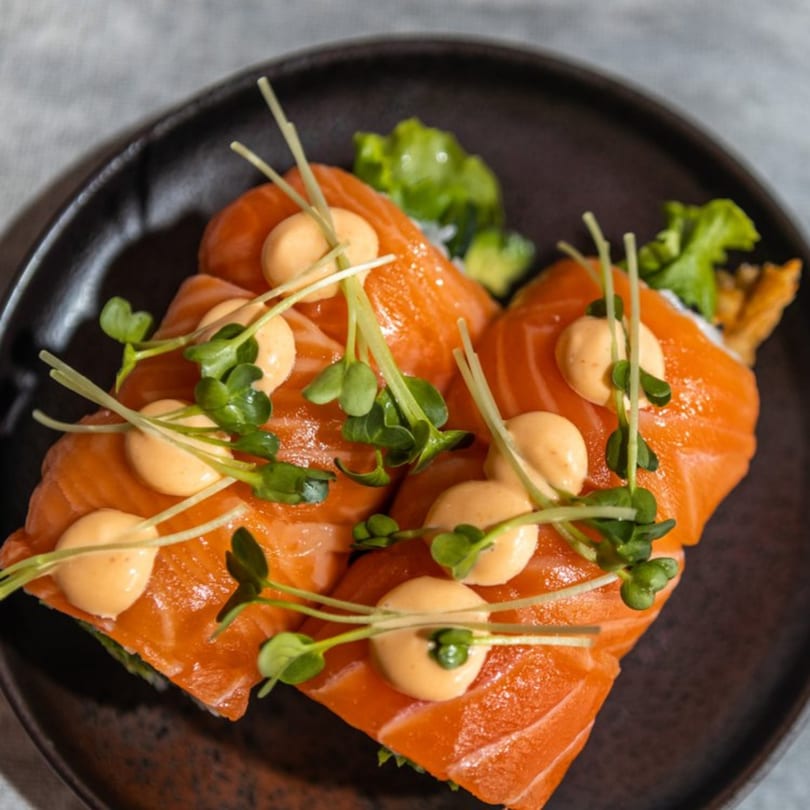 Iro Sushi's Stuff x Roll, featuring salmon, sauce, and microgreens on a dark plate.